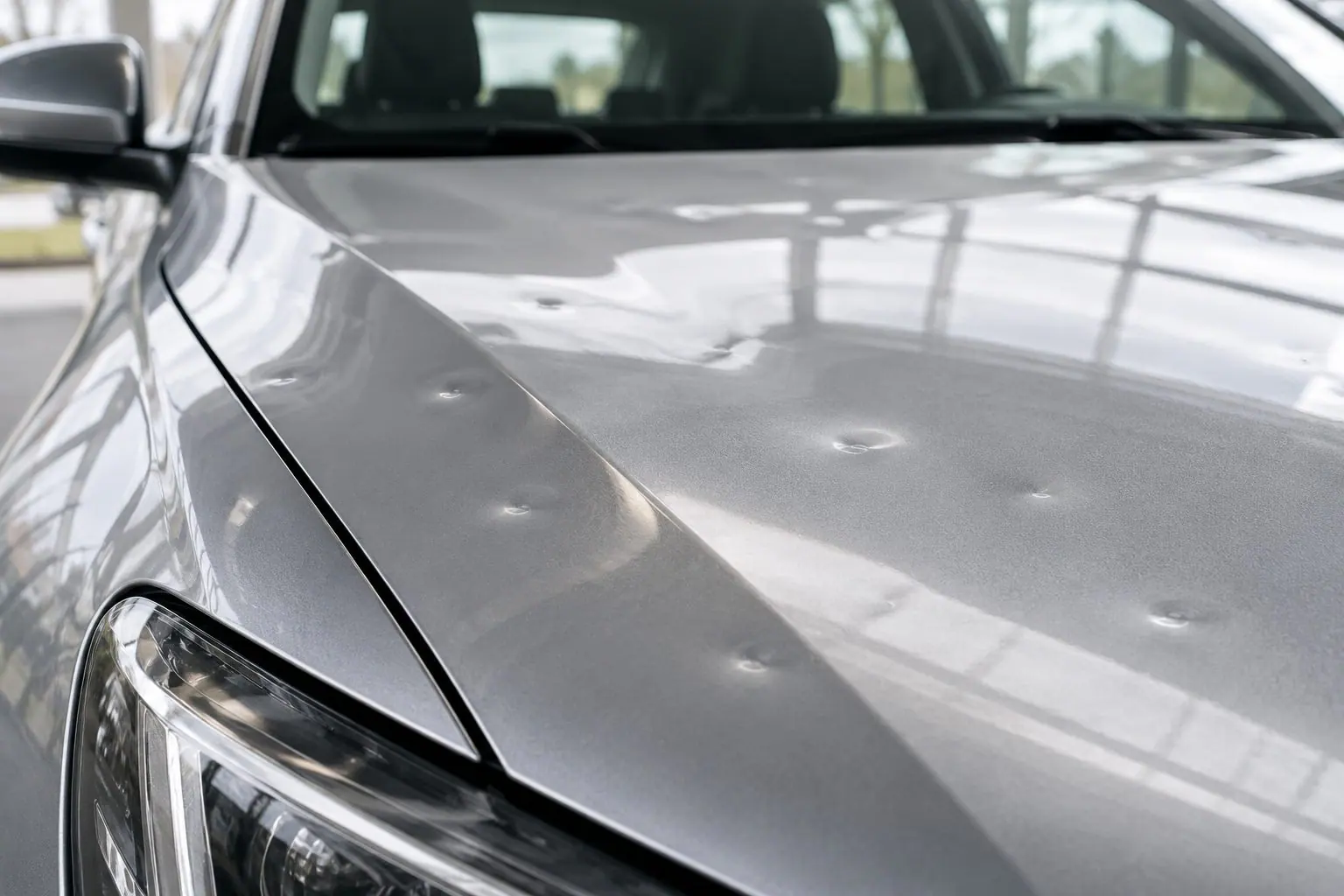 Motorhaube eines silbernen Pkw mit mehreren kleinen Hageldellen.