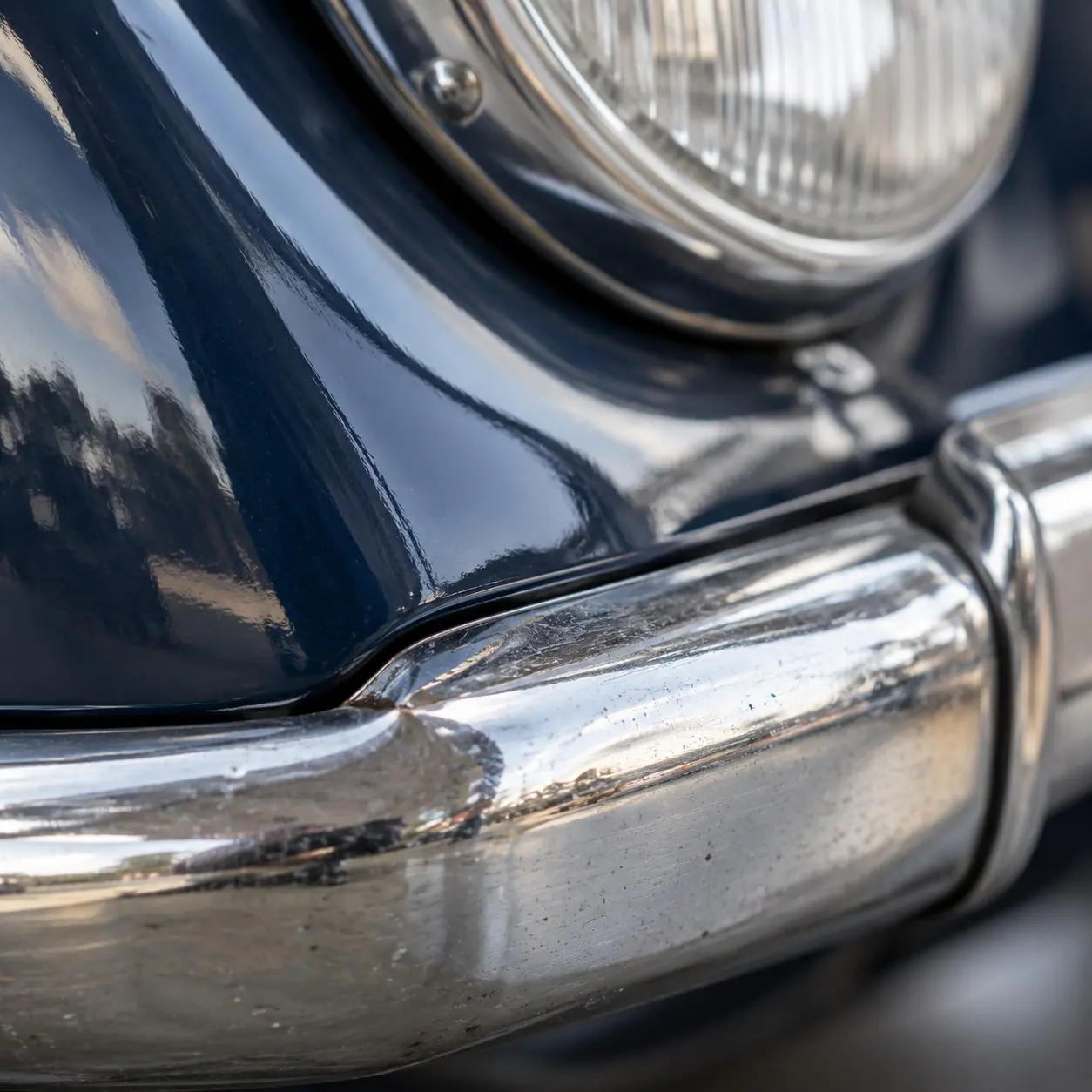 Chromstoßstange und dunkelblauer Kotflügel eines Oldtimers in Nahaufnahme.